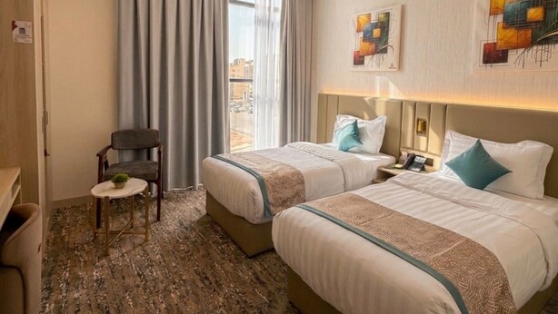 Ein Hotelzimmer mit zwei Betten, einem Sessel, einem kleinen Tisch und Blick auf die Stadt.