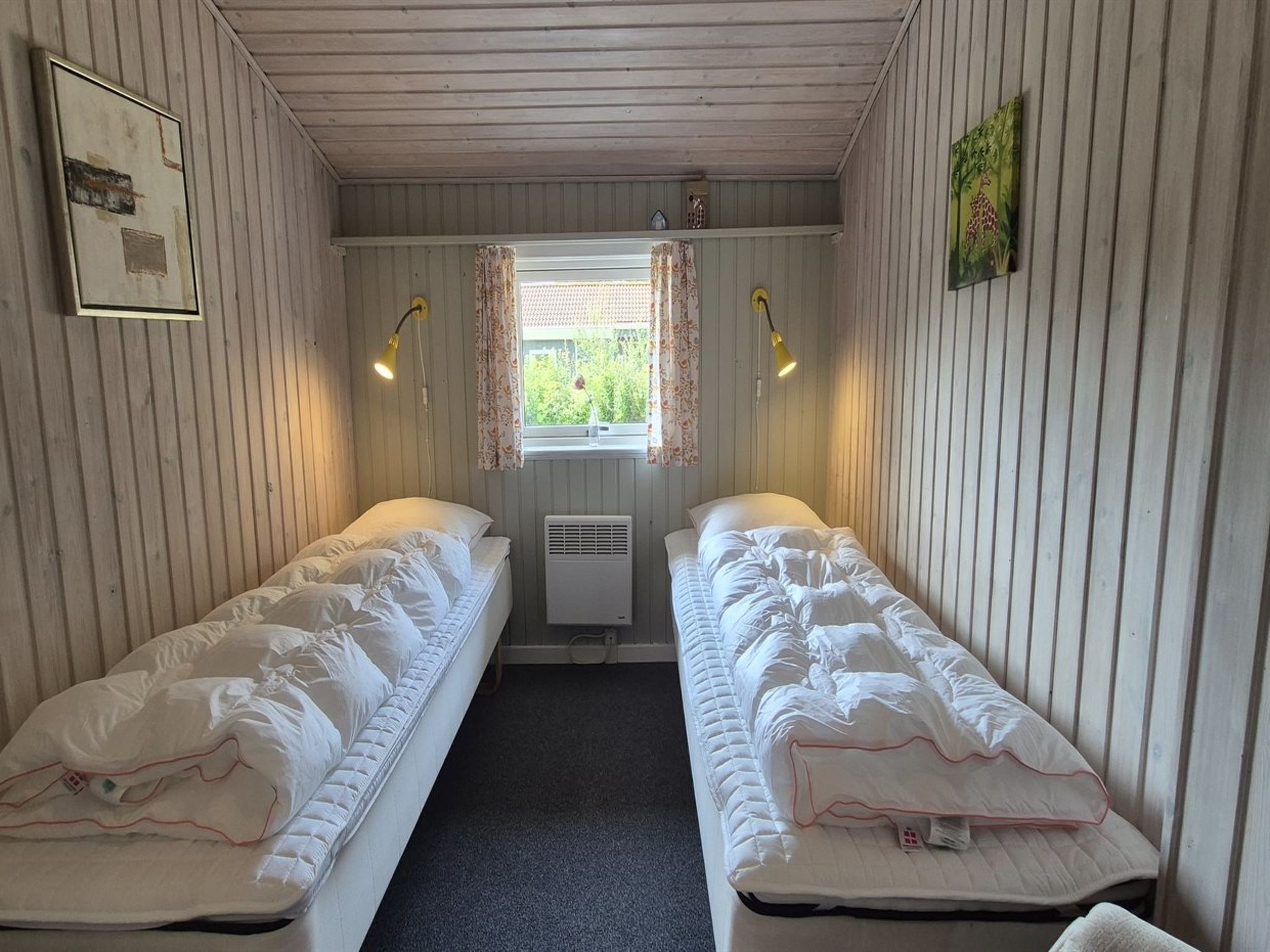 Une chambre avec deux lits simples, une fenêtre avec des rideaux, un radiateur et des lampes fixées au mur.