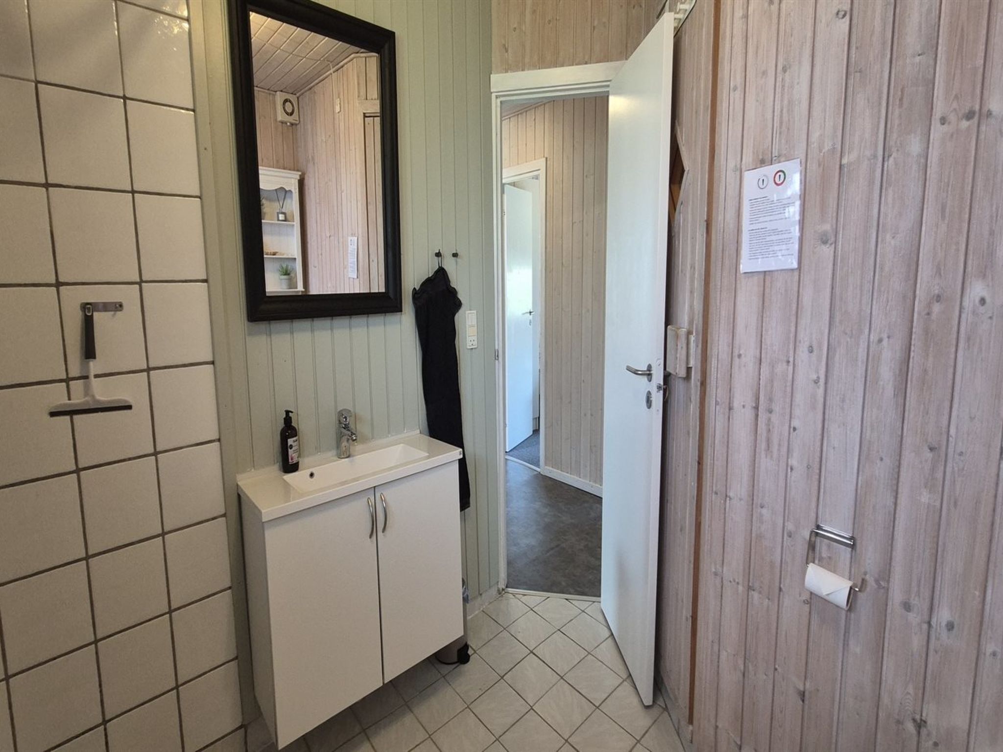 Een badkamer met een wit wastafelmeubel, spiegel en betegelde wanden.