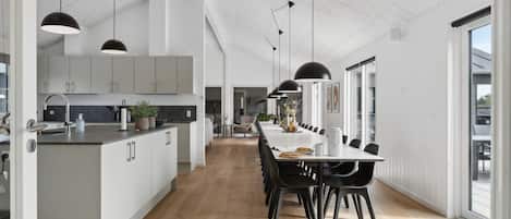 A modern kitchen with a central island, black pendant lighting, and a dining area with a long table and chairs.
