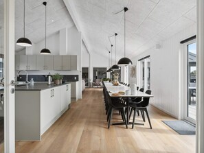 A modern kitchen with a central island, black pendant lighting, and a dining area with a long table and chairs. - 5 Star Holiday Home in Idestrup (Idestrup)