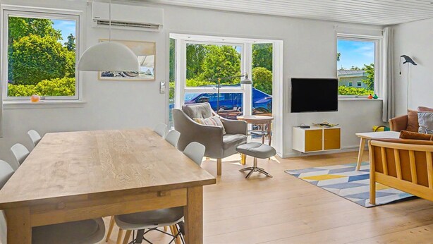 A modern living room with a wooden dining table, a sofa, a TV, and large windows with a view of greenery. - "Aderice" - 80m from the sea by Interhome (Haderslev)