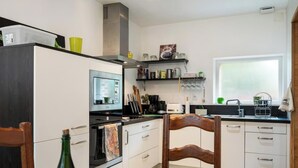 Ett kompakt kök med mikrovågsugn, ugn och kaffebryggare. Köket har skåp och ett fönster som släpper in naturligt ljus.