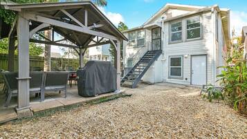 A covered patio area with outdoor furniture, a barbecue grill, and a gravel ground.