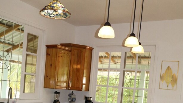 Una cocina con armarios de madera, una isla grande con taburetes, luces colgantes y una ventana con vistas.