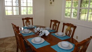 Comedor con una mesa de madera dispuesta para seis personas, rodeada de sillas, y un ventanal que ofrece vistas a la vegetación.
