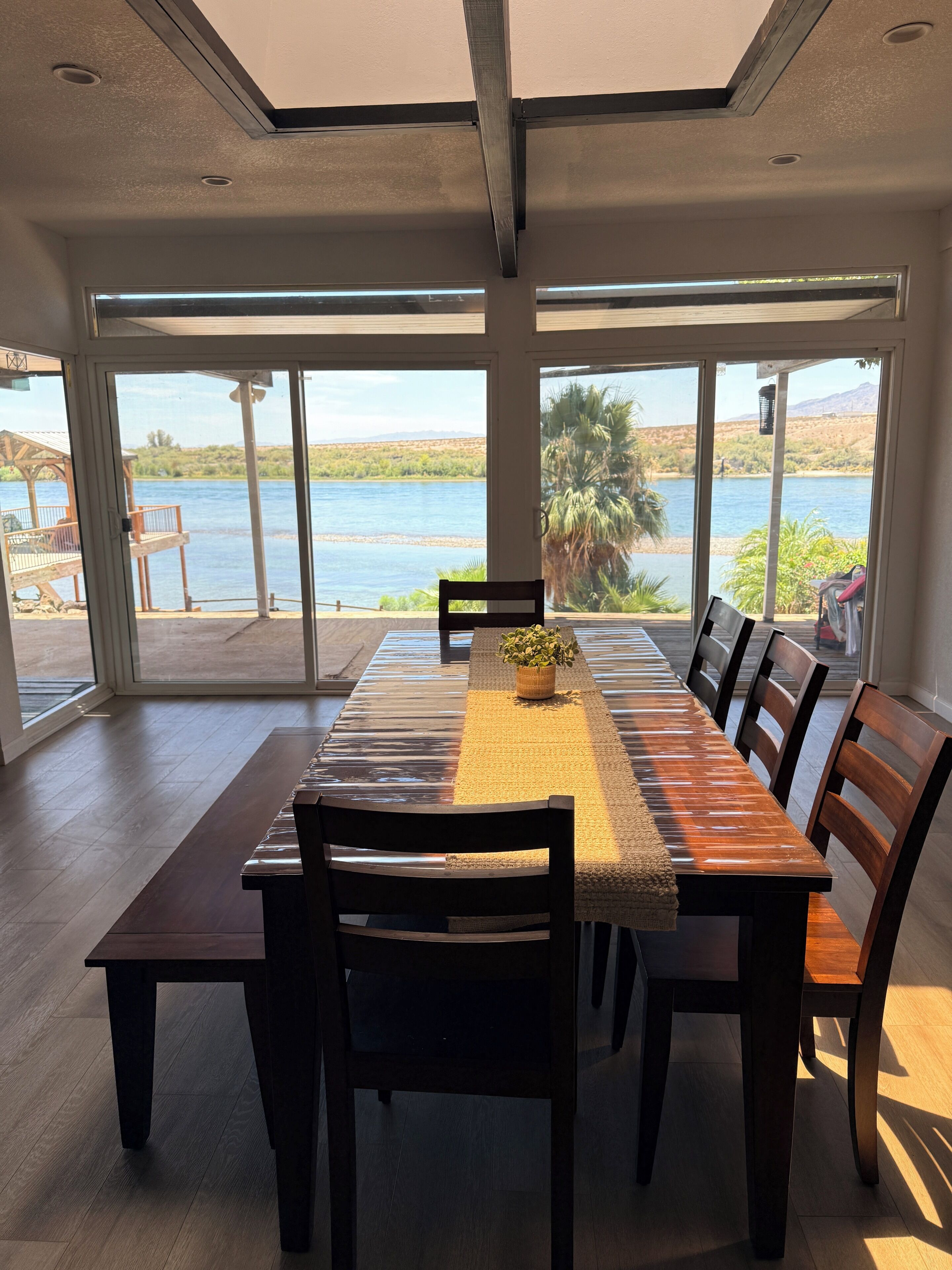 Comedor con una mesa larga, sillas y vista a una masa de agua a través de amplios ventanales.