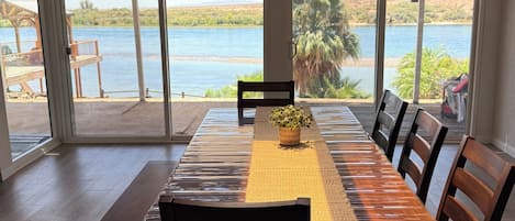 Comedor con una mesa larga, sillas y vista a una masa de agua a través de amplios ventanales.