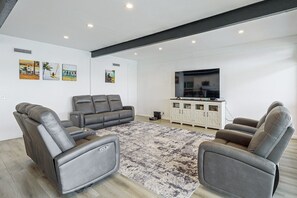 A modern living room with a gray sofa set, a flat-screen TV on a white cabinet, and artwork on the walls.