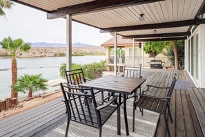 An outdoor patio with a table and chairs, overlooking a body of water and a mountainous landscape.