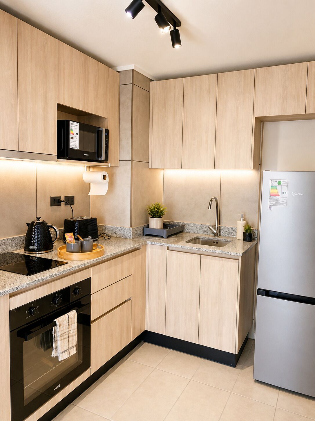 Una cocina moderna con armarios de madera, microondas, hervidor, tostadora, pileta y refrigerador.