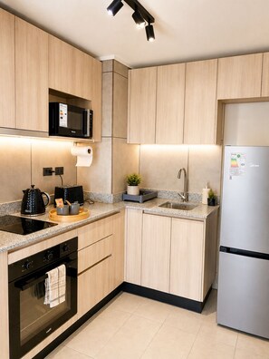 A modern kitchen with wooden cabinets, a microwave, a kettle, a toaster, a sink, and a refrigerator. - New apartment, one step away from everything. (La Florida)
