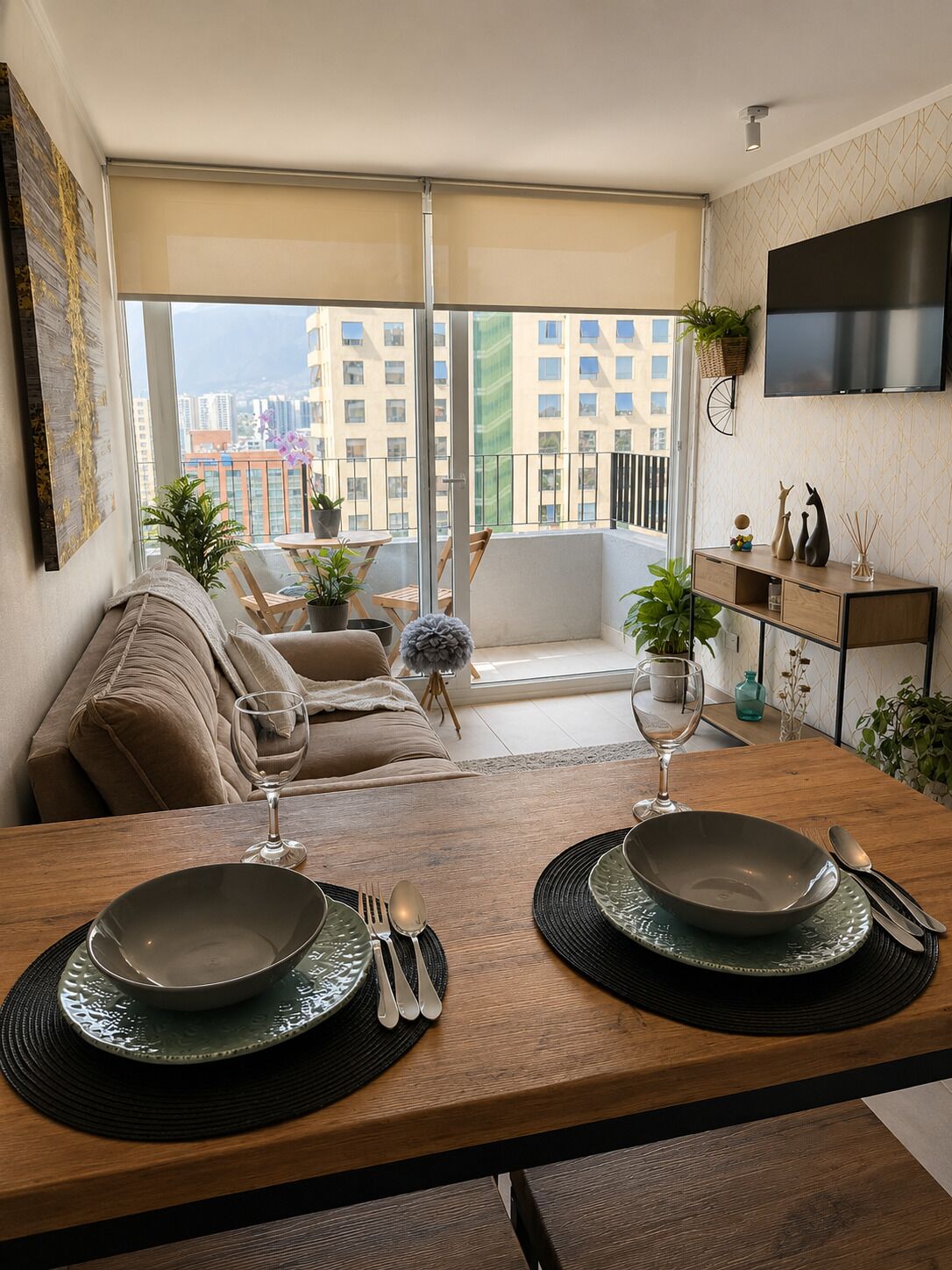 Un comedor con una mesa preparada para dos personas, un sofá y un balcón con vista a la ciudad.