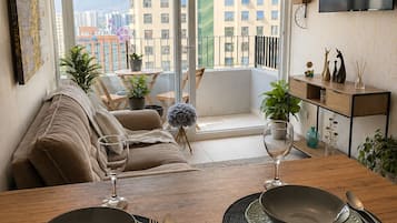 Un comedor con una mesa preparada para dos personas, un sofá y un balcón con vista a la ciudad.