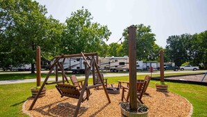 A playground with swings and seating, surrounded by mulch and grass, with RVs in the background.