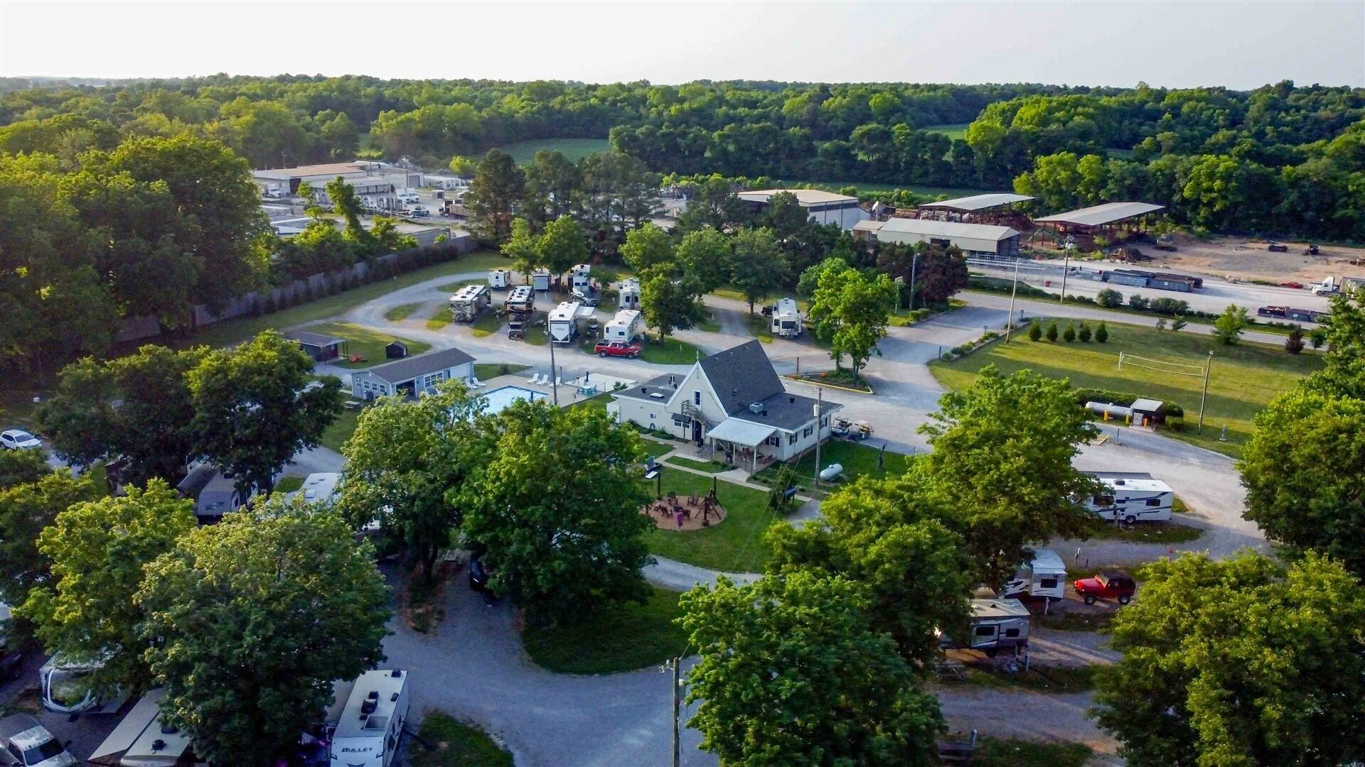 Vista aérea de un camping con vehículos recreativos, un edificio blanco grande y vegetación circundante.