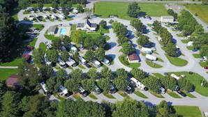 An aerial view of a campground with RVs and trailers parked in organized rows, surrounded by trees and green spaces.