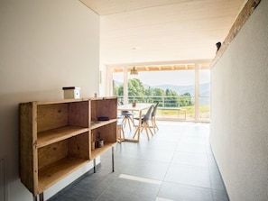 A modern interior with a wooden shelf unit, a dining area with chairs, and a large window offering a view of the outdoors. - Appartements - Ferme La Joux-Chaupe, (St-Ursanne), by Interhome (Saint-Ursanne)