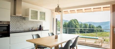 A modern kitchen with a dining area, large windows, and a view of the outdoors.