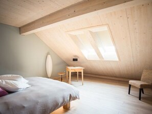 Una habitación con techo inclinado, una cama, una silla y una mesita.