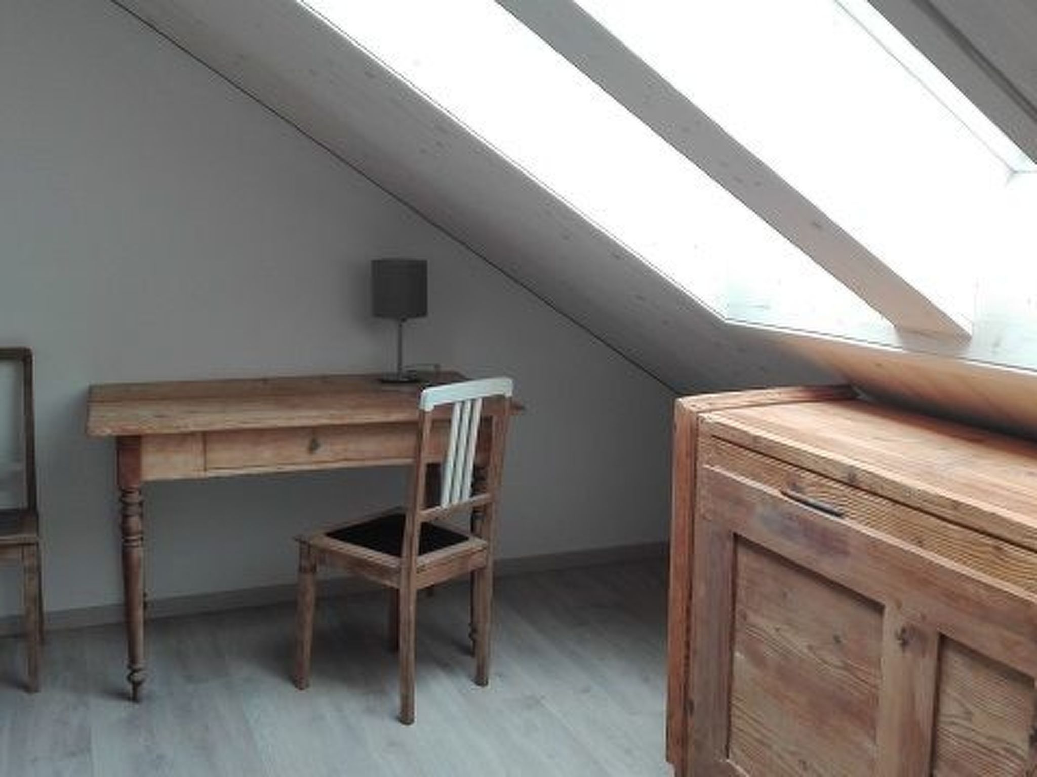 Una habitación con techo inclinado, un escritorio de madera, una silla y un armario.