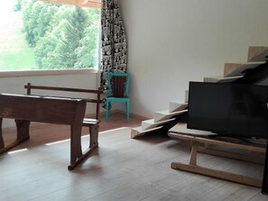 Una habitación con un banco de madera, una silla color turquesa y un televisor sobre un mueble.