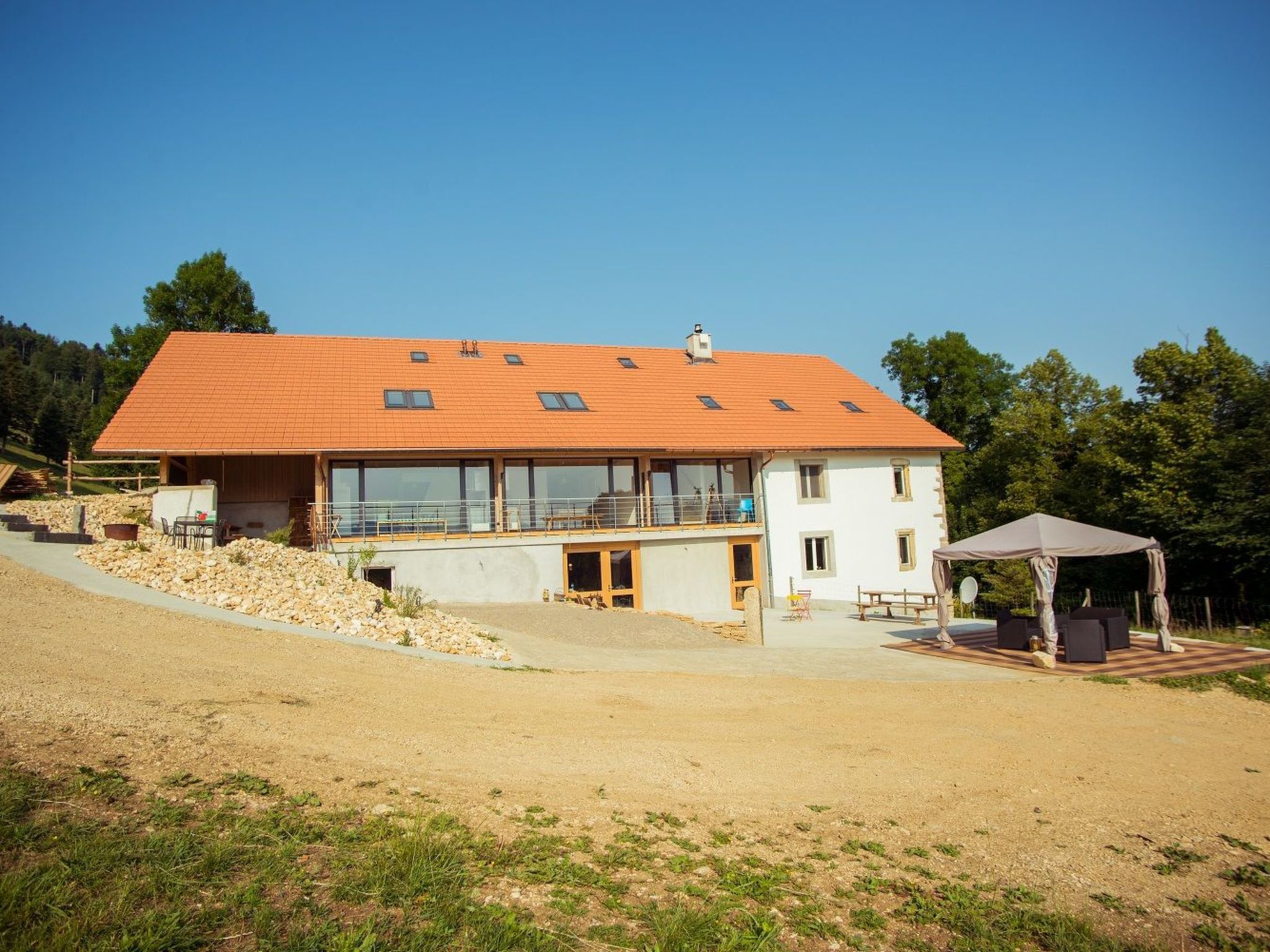 Ein zweistöckiges Haus mit geneigtem Dach, großen Fenstern und einer überdachten Außenbereich-Sitzgelegenheit.