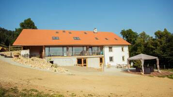 Ein zweistöckiges Haus mit geneigtem Dach, großen Fenstern und einer überdachten Außenbereich-Sitzgelegenheit.
