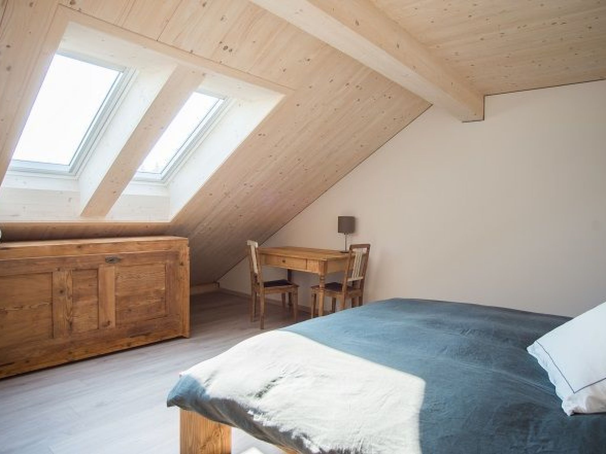 Une pièce avec un plafond en pente, des meubles en bois, un lit et des fenêtres de toit.