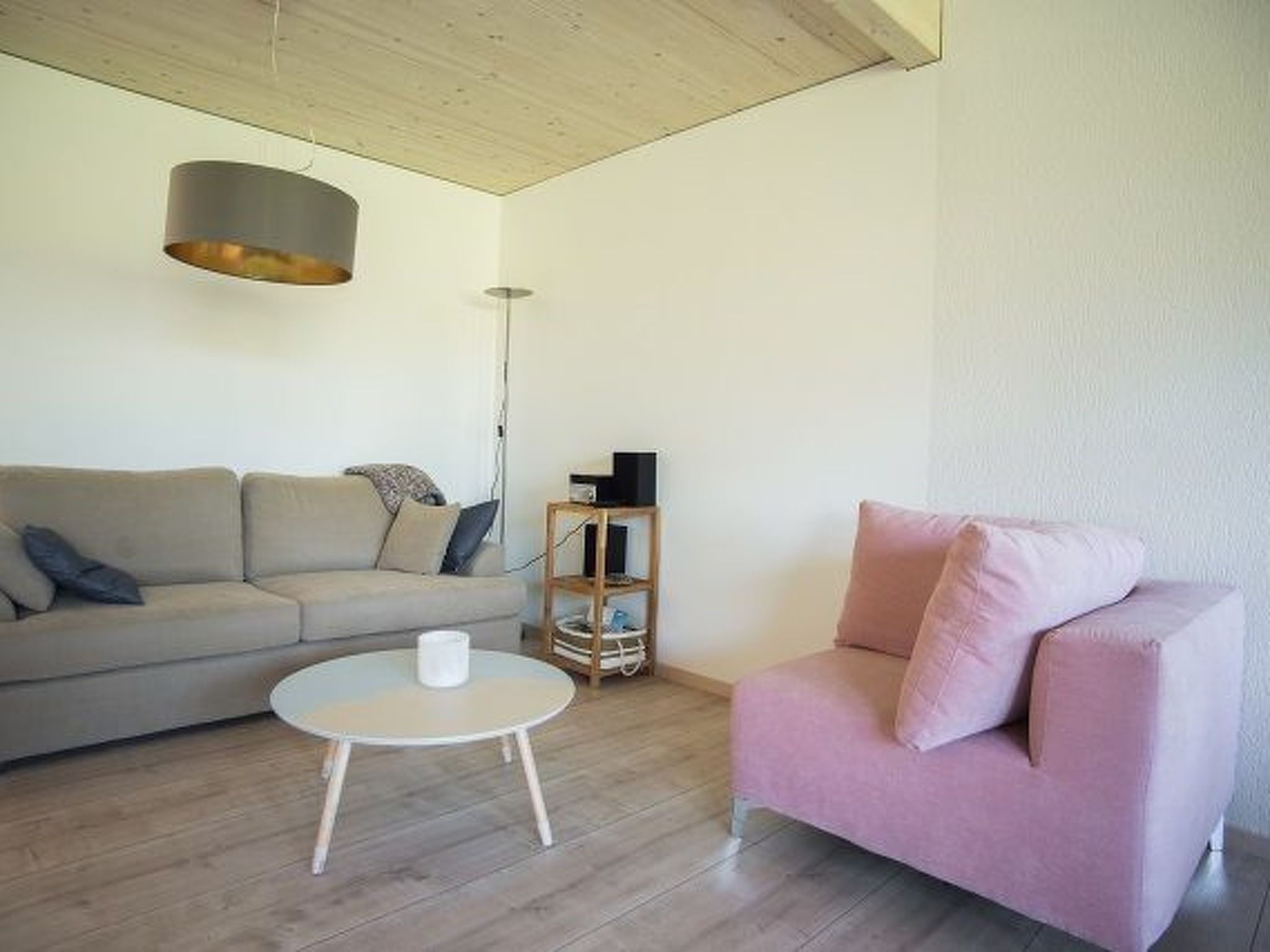 Ein Wohnzimmer mit einer Couch, einem rosa Sessel, einem runden Couchtisch und Holzboden.