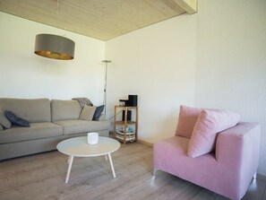 Una sala de estar con un sofá, un sillón rosa, una mesa de centro redonda y suelo de madera.