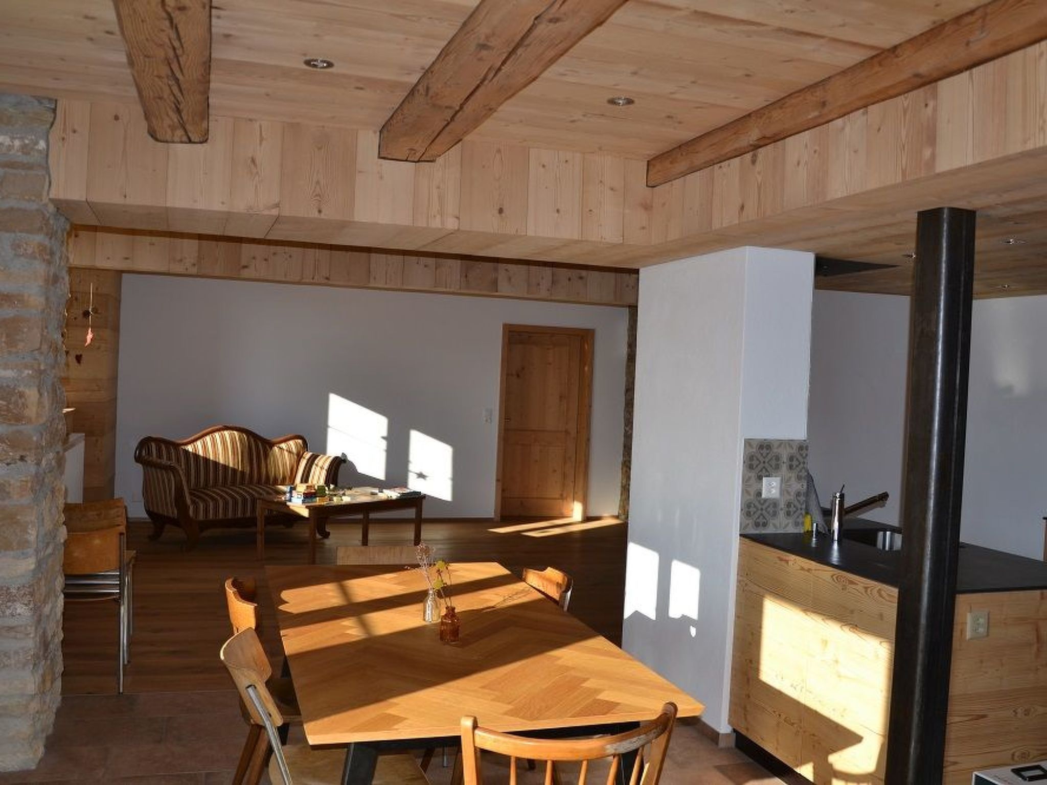 A spacious living area with a wooden dining table, a sofa, and a kitchen area with a sink.