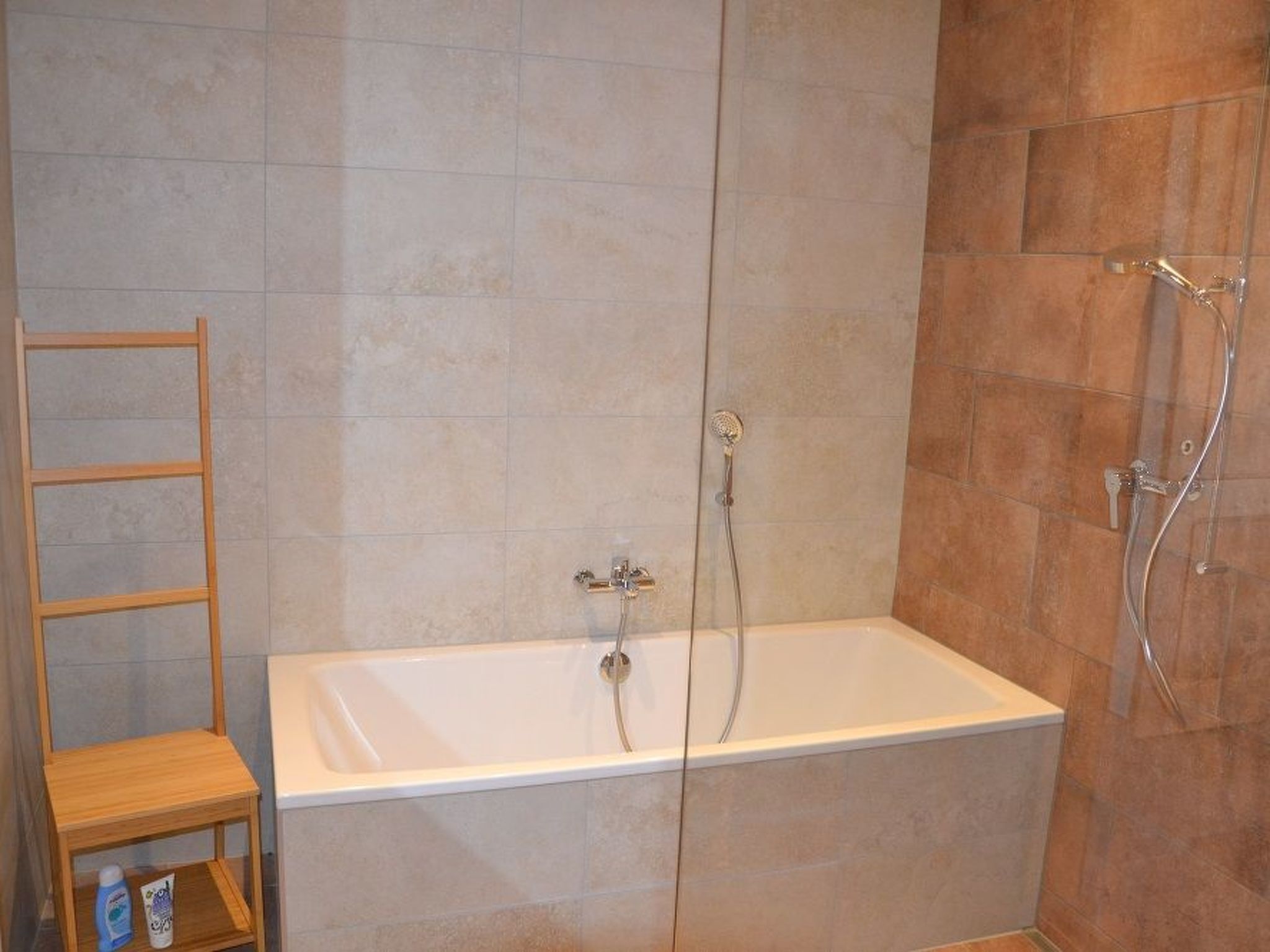Une salle de bain avec une baignoire, une douche et une étagère en bois où sont rangés les articles de toilette.