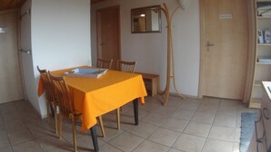 A dining area with a table covered in a yellow tablecloth, wooden chairs, a wooden ceiling, a door, and a mirror on the wall.
