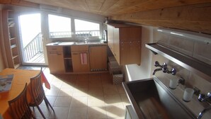 A compact kitchen with wooden ceiling, a dining area with chairs, and a view to the outside.