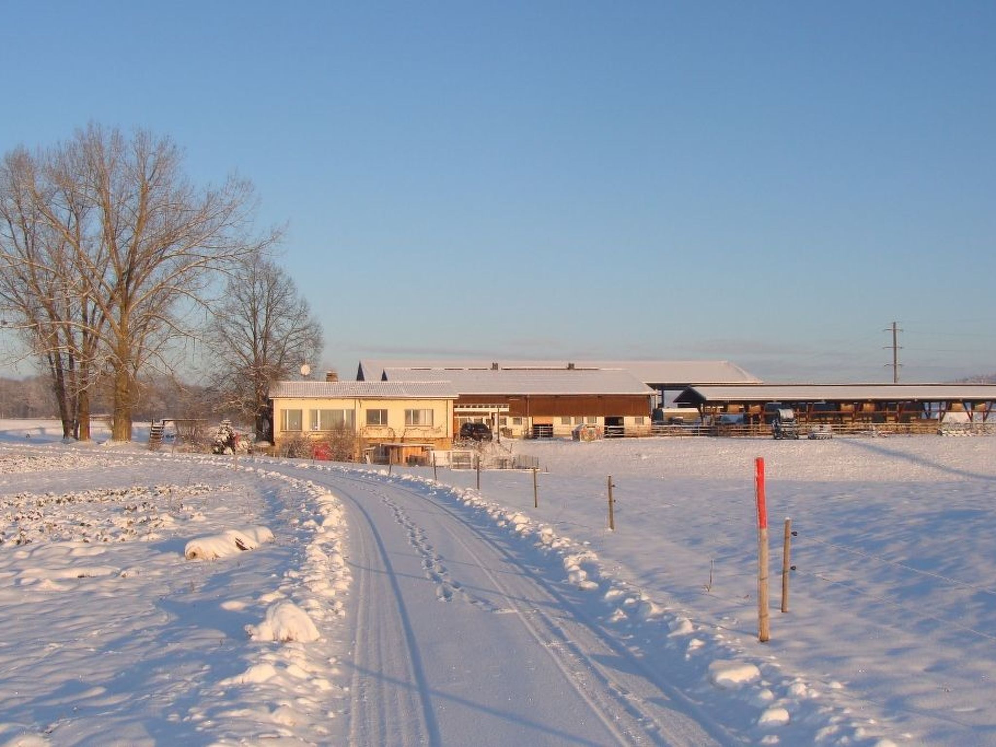 Schneebedeckte Landschaft mit einem Gebäude, das ein flaches Dach und einen umzäunten Hof hat.