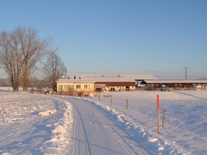 A snow-covered landscape with a building that has a flat roof and a fenced yard.