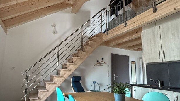 A modern kitchen with a wooden staircase, teal chairs, and a dining table. - Gîtes - La Clef des Franches, (Saignelegier), by Interhome (Saignelegier)