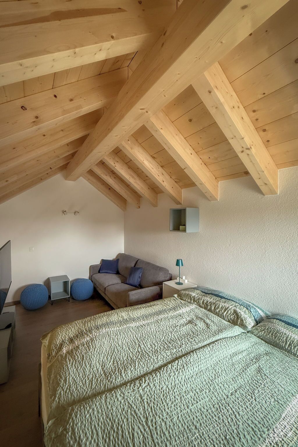 Ein Schlafzimmer mit schrägverdeckter Decke, einem Bett, einer Couch, einem kleinen Tisch und einem an der Wand befestigten Regal.