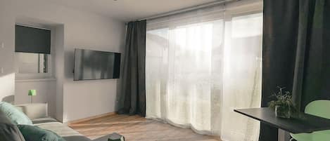 A modern living room with a flat-screen TV, a sofa, a coffee table, and a dining area with a table and chairs.