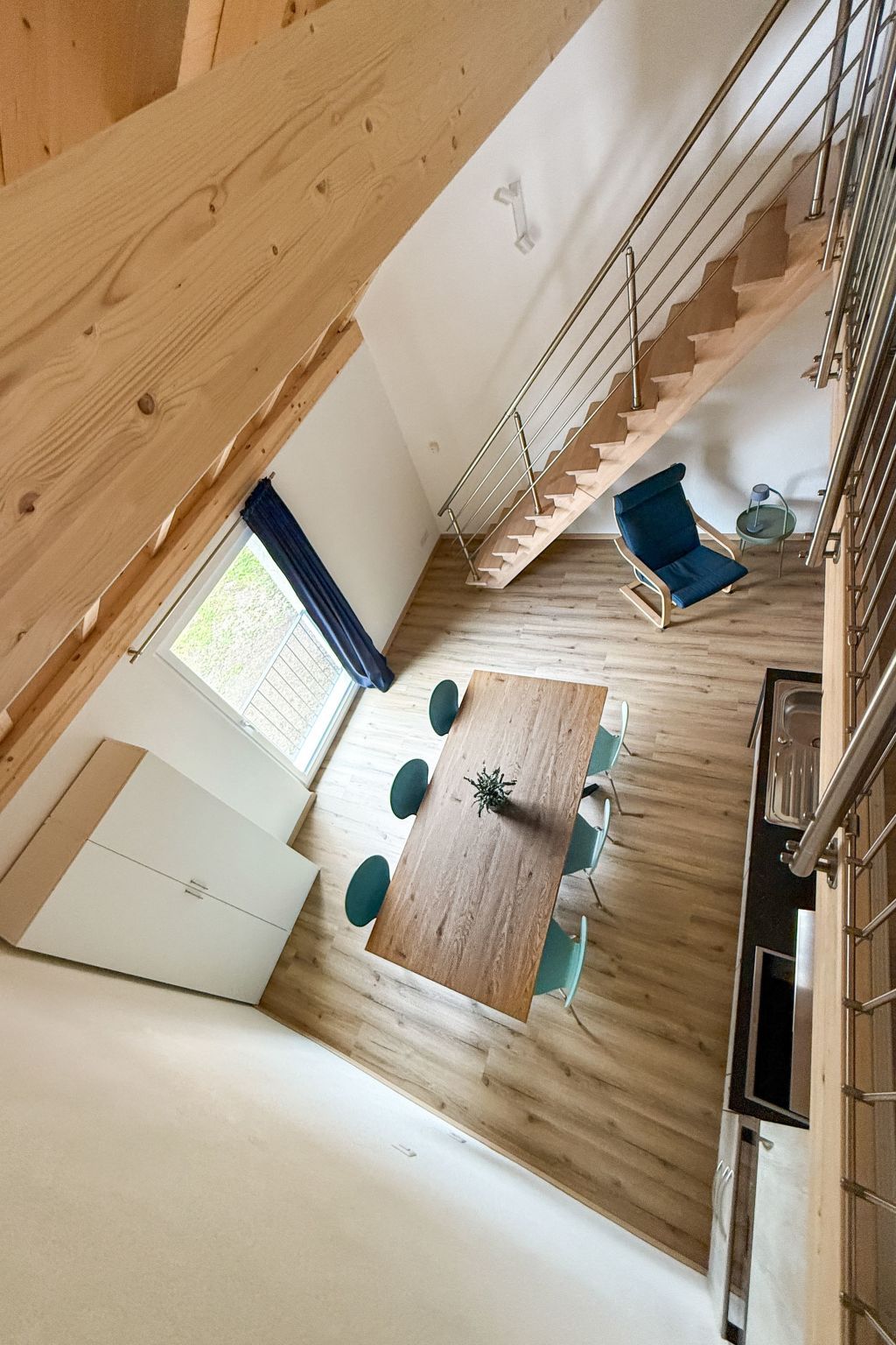 Un intérieur moderne avec un plancher en bois, une table à manger avec des chaises, un escalier et un canapé bleu.