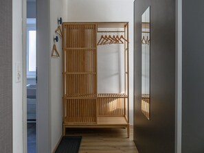 Ein begehbarer Kleiderschrank mit Holztüren, die sich nach innen schieben lassen, einer Kleiderstange und einem Spiegel an der Wand.