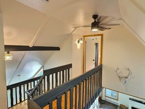 A staircase with wooden railings, a ceiling fan, and a mounted deer head on the wall.