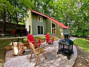 Una terraza de madera con sillas Adirondack, una parrilla y un edificio con techo rojo.