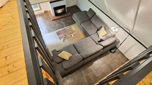 A modern living room with a sectional sofa, a fireplace, and a glass railing overlooking the space. - Chalets Cheribourg - Le 144 - Spa (Orford)