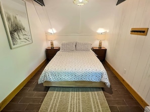 A bedroom with a bed, two bedside tables with lamps, a rug, and a wall-mounted light fixture. - Chalets Cheribourg - Le 144 - Spa (Orford)