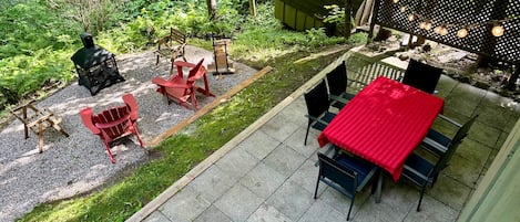 A patio with a red table and chairs, a wooden deck, and a garden area with trees and a grill.