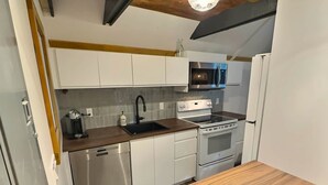 A compact kitchen with white cabinets, a stainless steel dishwasher, a built-in oven, and a microwave. - Chalets Cheribourg - Le 144 - Spa (Orford)