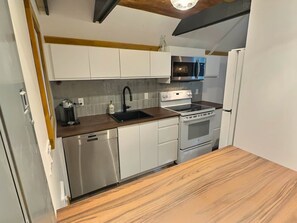 A compact kitchen with white cabinets, a stainless steel dishwasher, a built-in oven, and a microwave. - Chalets Cheribourg - Le 144 - Spa (Orford)