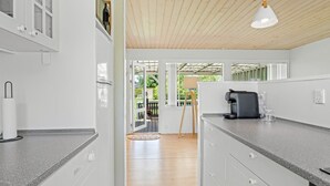 A modern kitchen with white cabinetry, a coffee machine, and a wooden ceiling. - "Gertraud" - 600m from the sea by Interhome (Væggerløse)